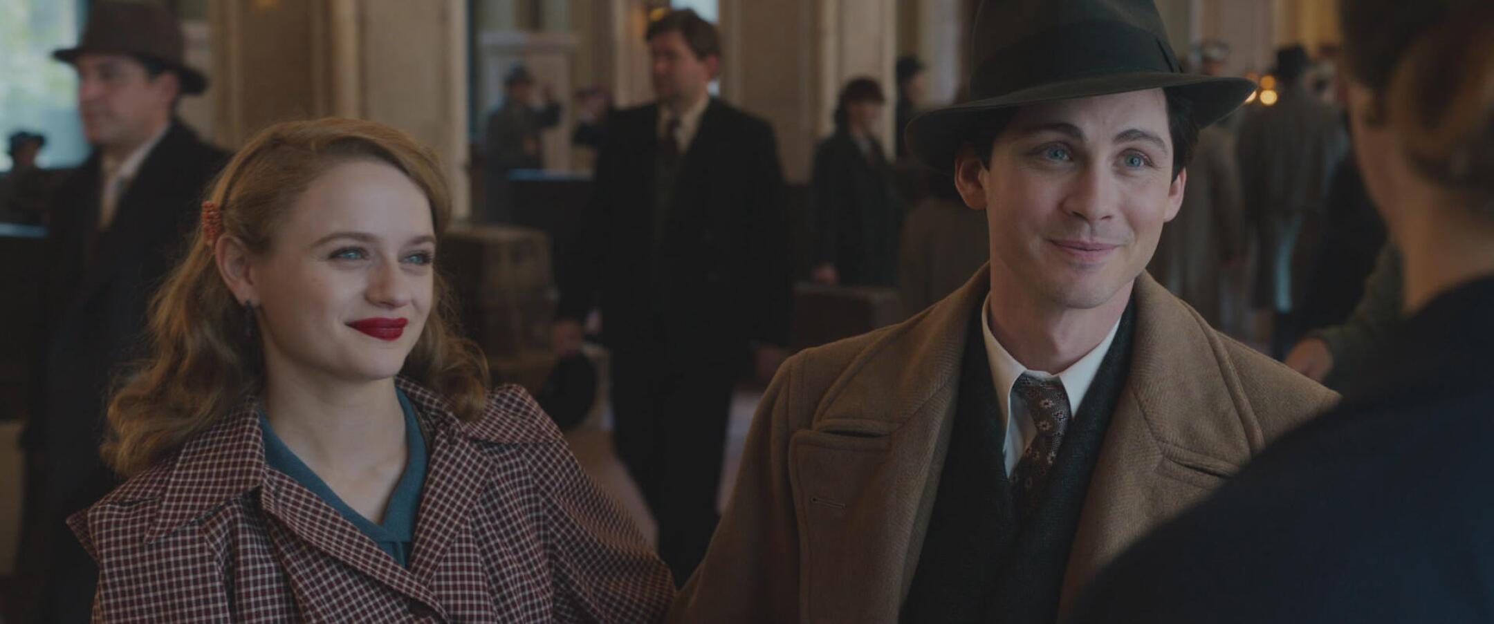 A young man and woman in period clothing smile at someone in a scene from 