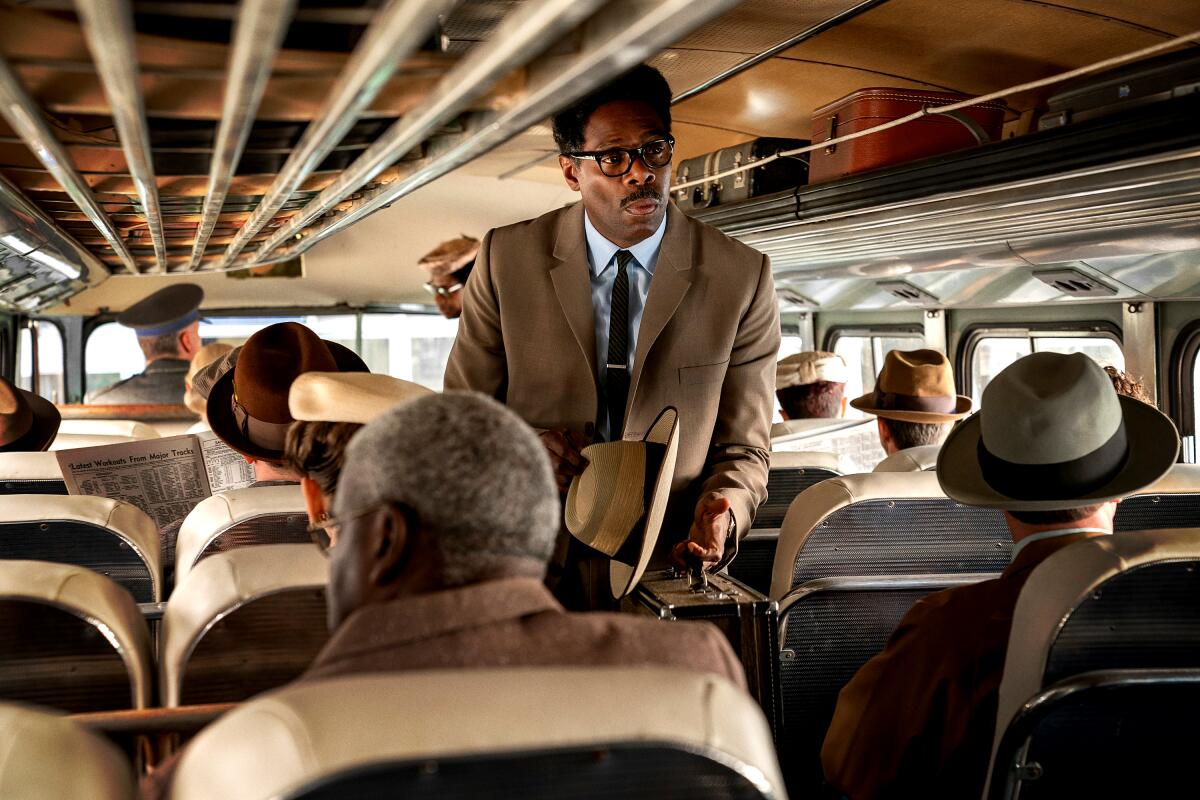 A man in a suit walks down the aisle of a bus in 
