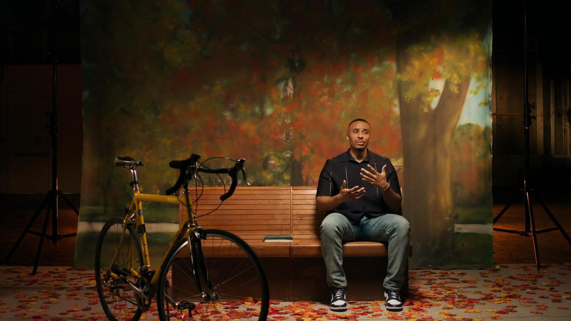 A man sits on a bench with a bicycle nearby in 
