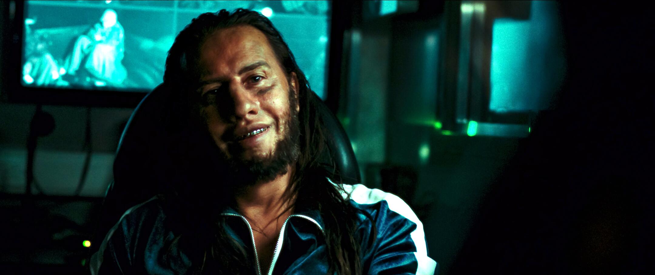 A man with long hair and metal teeth in a scene from 