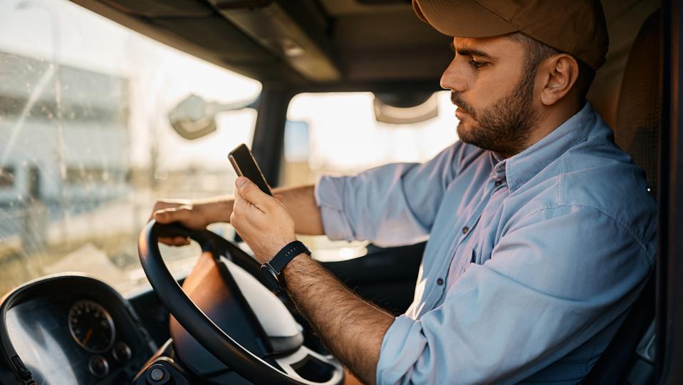 Side view of truck driver reading text message on smart phone while driving.