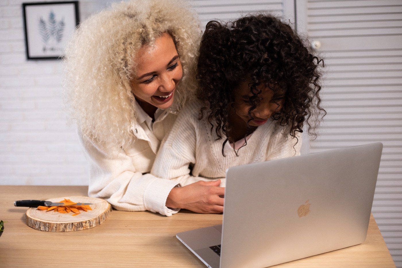 Laughing black mother and daughter browsing modern laptop in kitchen