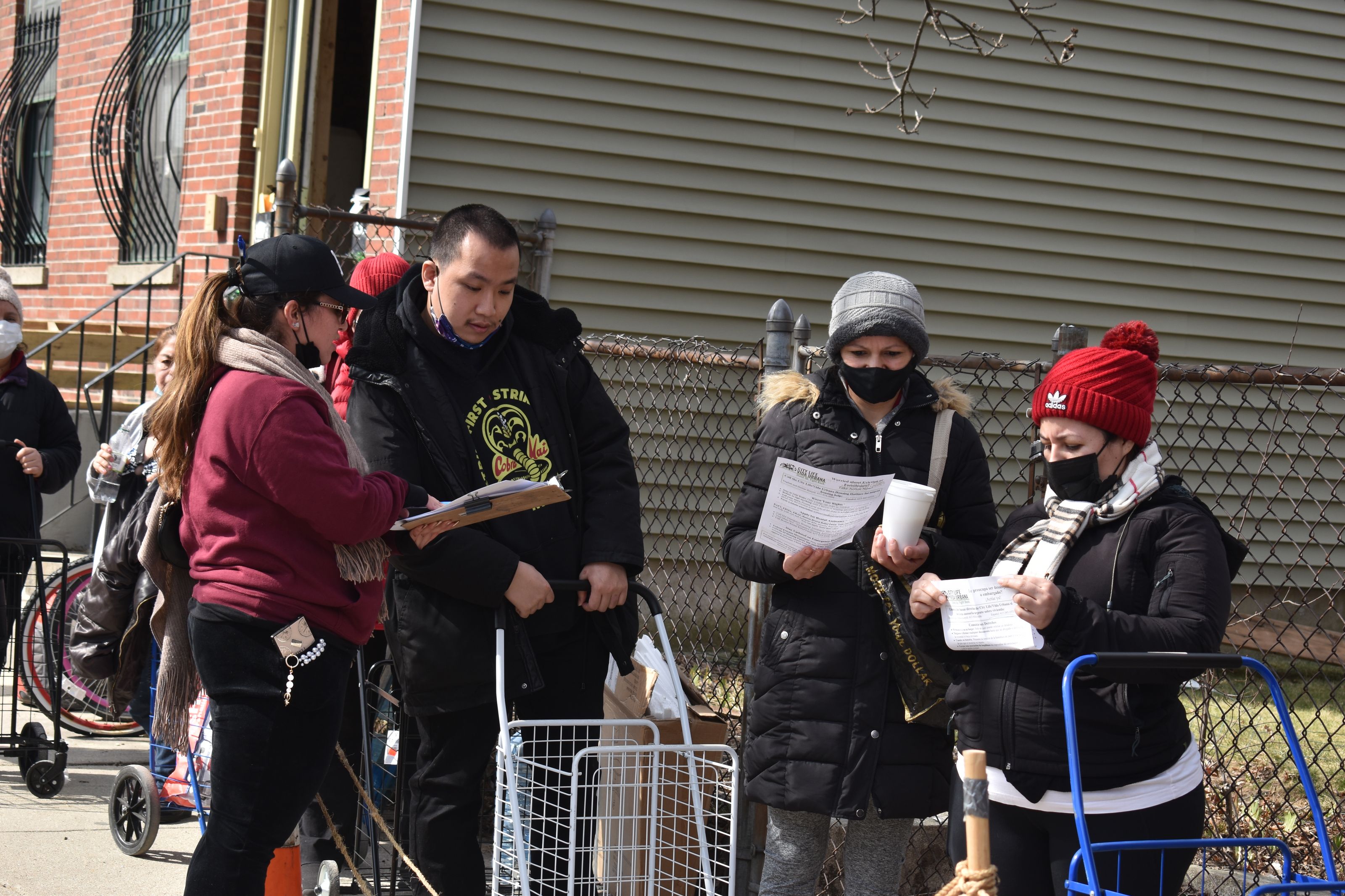 Representatives from Urbana Vida, which canvases for signatures to prevent the eviction of an apartment building scheduled for demolition, talk to clients in line at East Boston Community Soup Kitchen, March 15, 2022 (Photo credit: Brandon Hill).