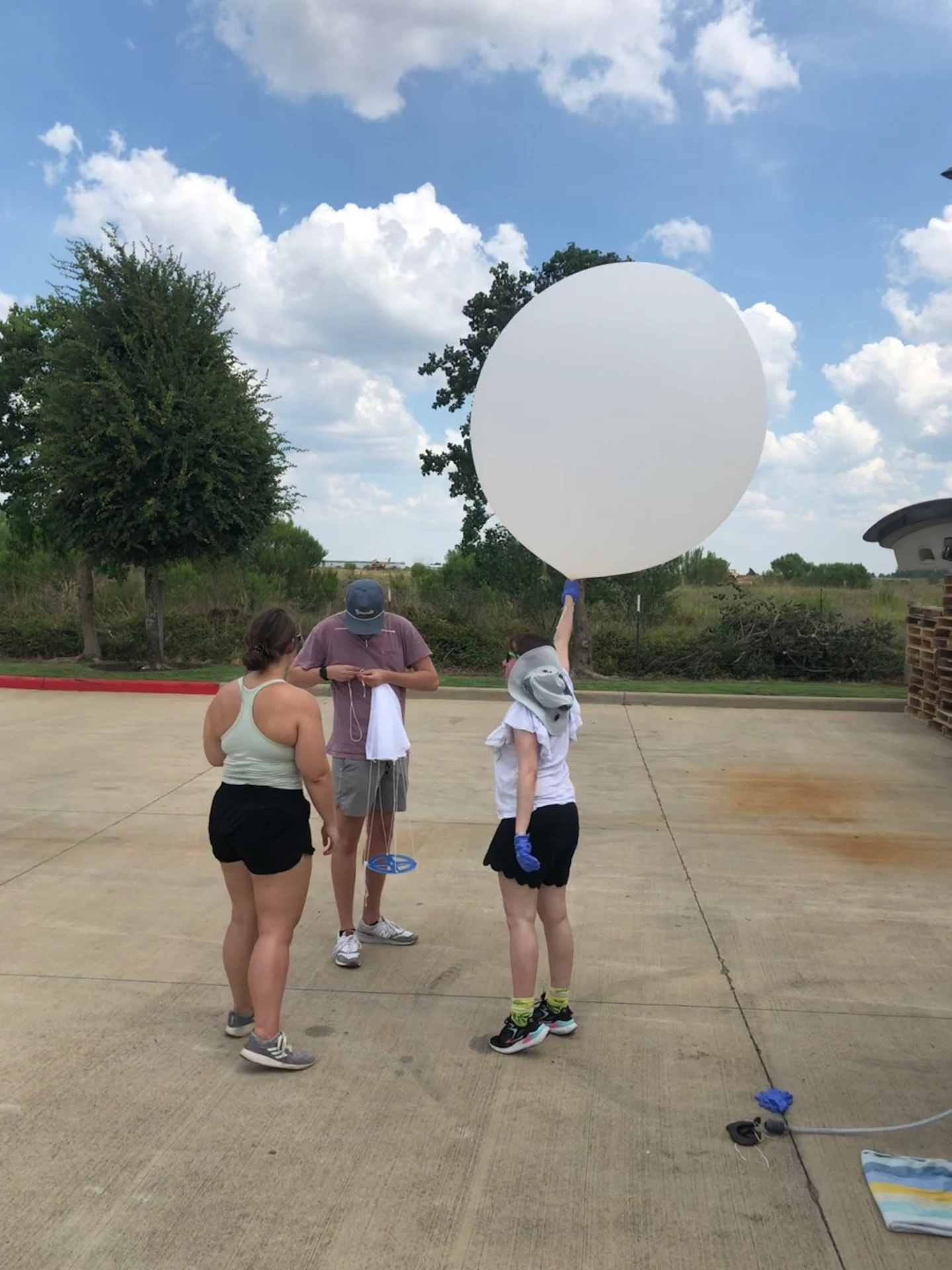 An image of three people standing on a concrete surface holding a large white weather balloon.