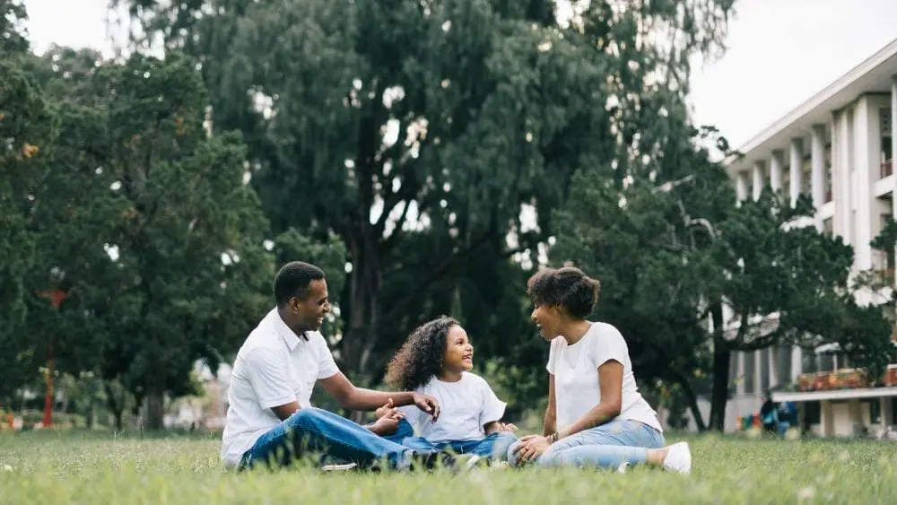 Family of three sitting in grass.