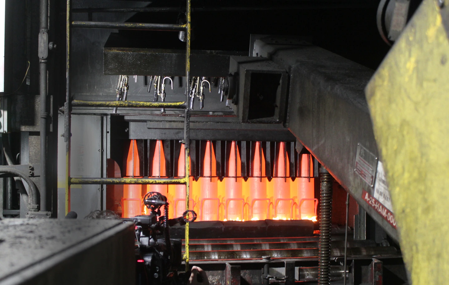 Ammunition shells come out of a furnace, in a bright red color.