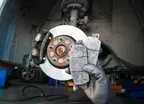 Used car brake pads in the hands of a mechanic with brake discs and brake calipers on the background