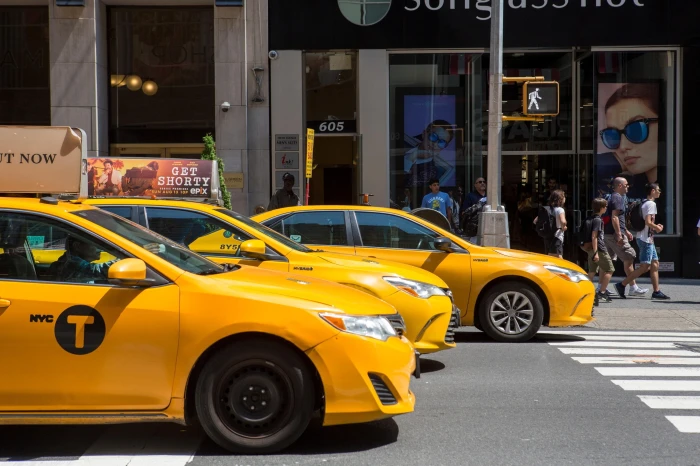Yellow NYC taxis lined up at a crosswalk as pedestrians walk by