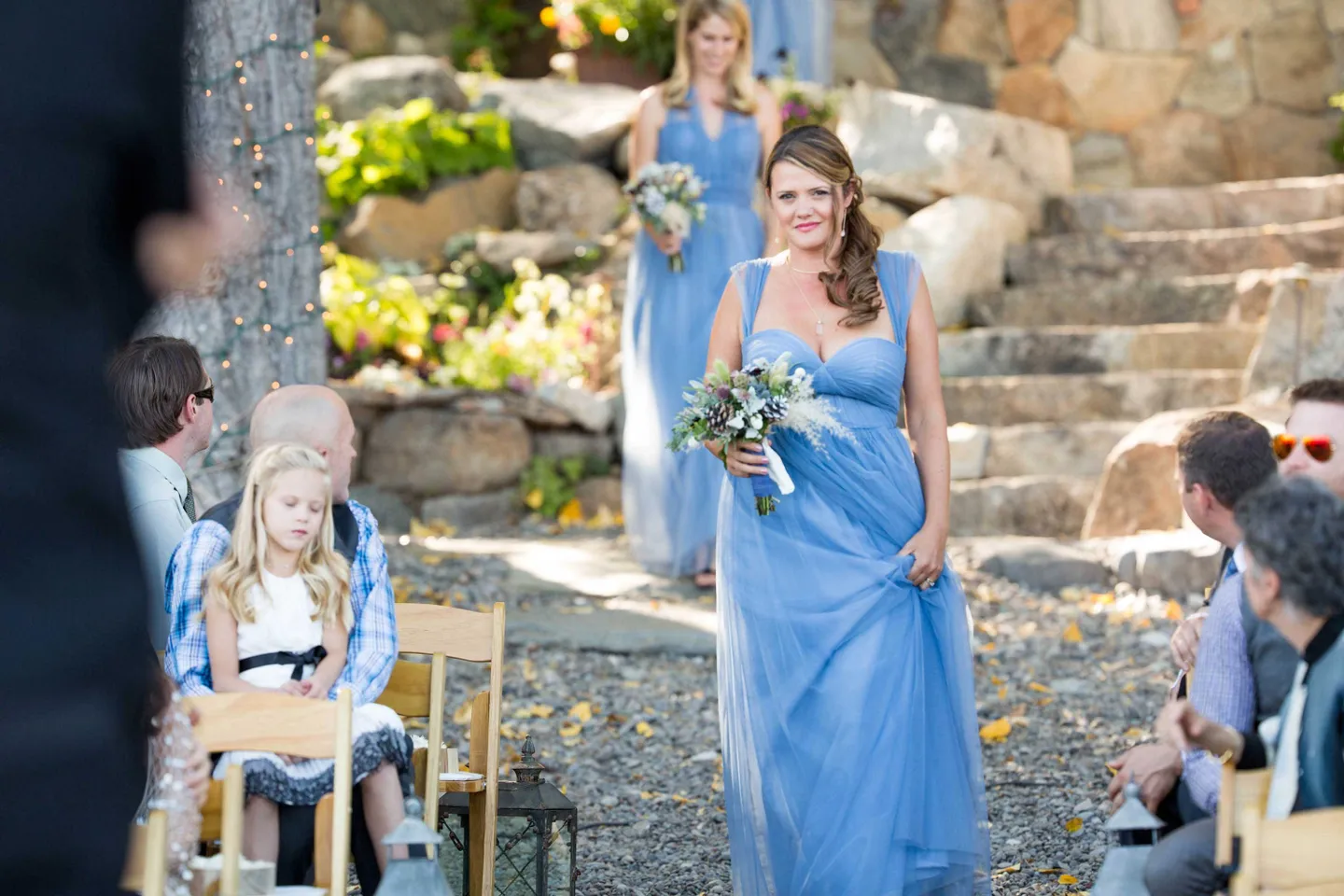 bridesmaids-dressed-in-blue-walk-down-stone-and-gravel-aisle