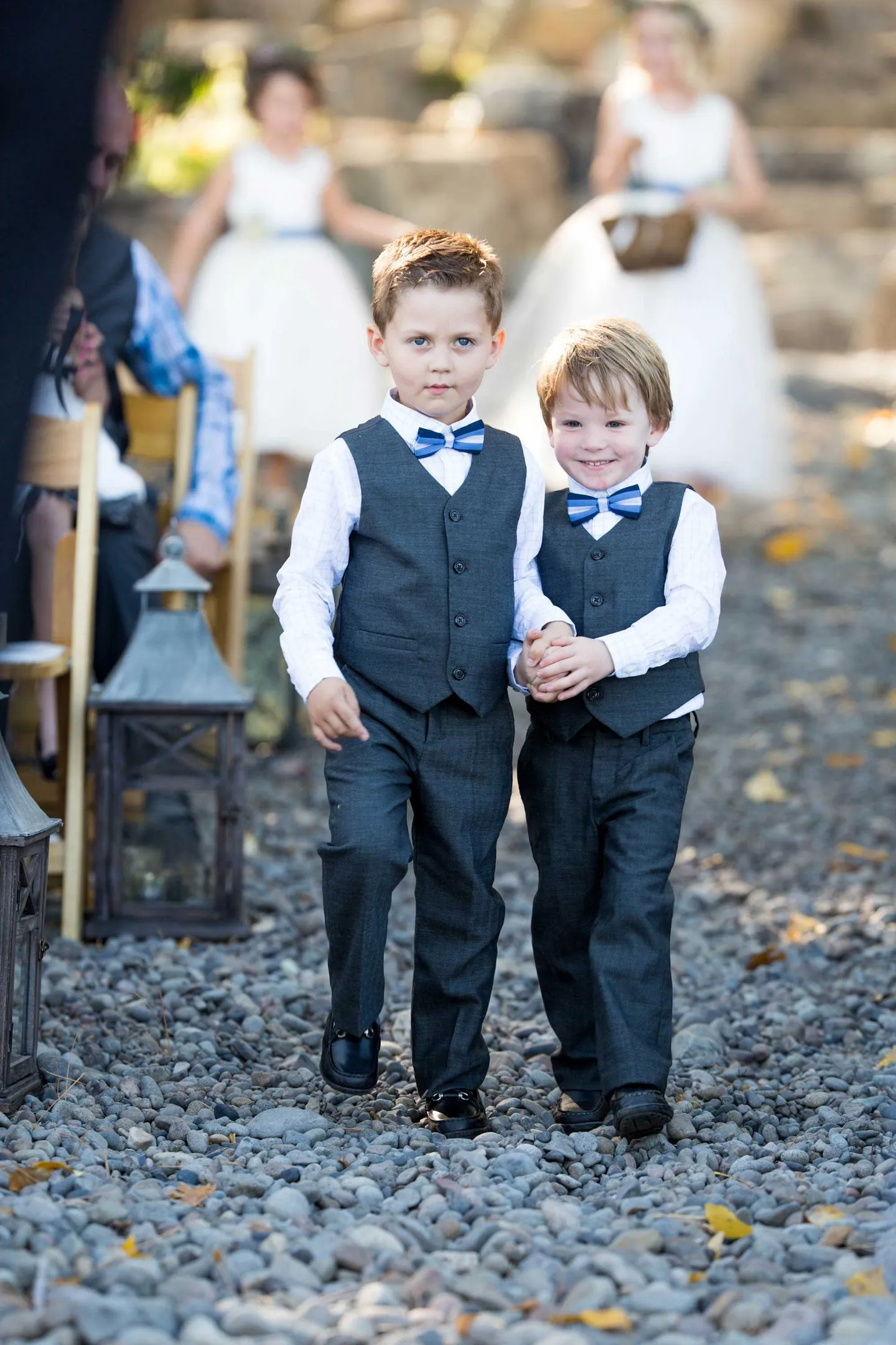 ring-bearers-in-grey-vets-and-blue-bow-ties-hold-hands-while-walking-down-the-aisle
