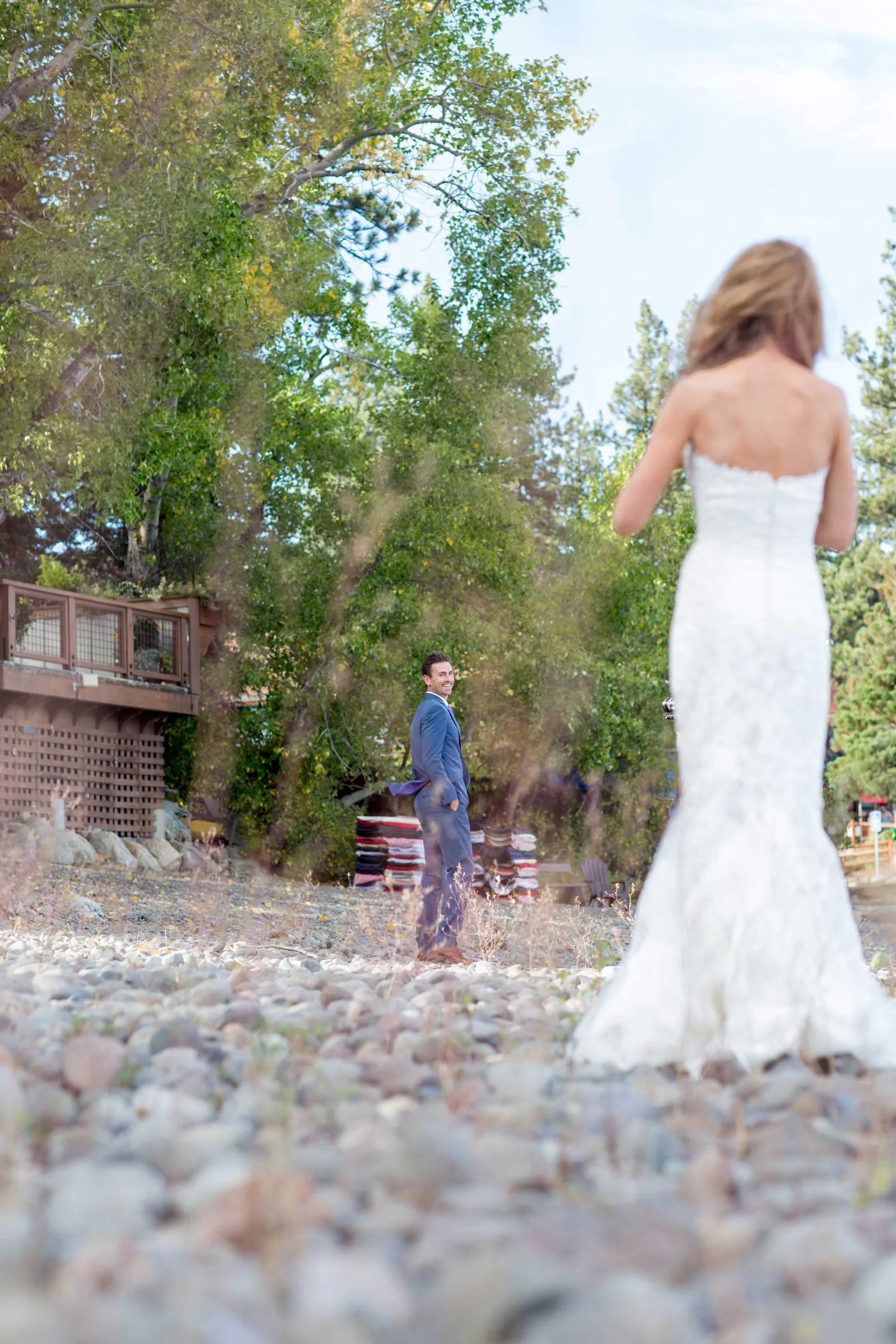 groom-turns-around-to-see-his-bride-during-first-look-blue-suit-white-dress-pebbles-forest