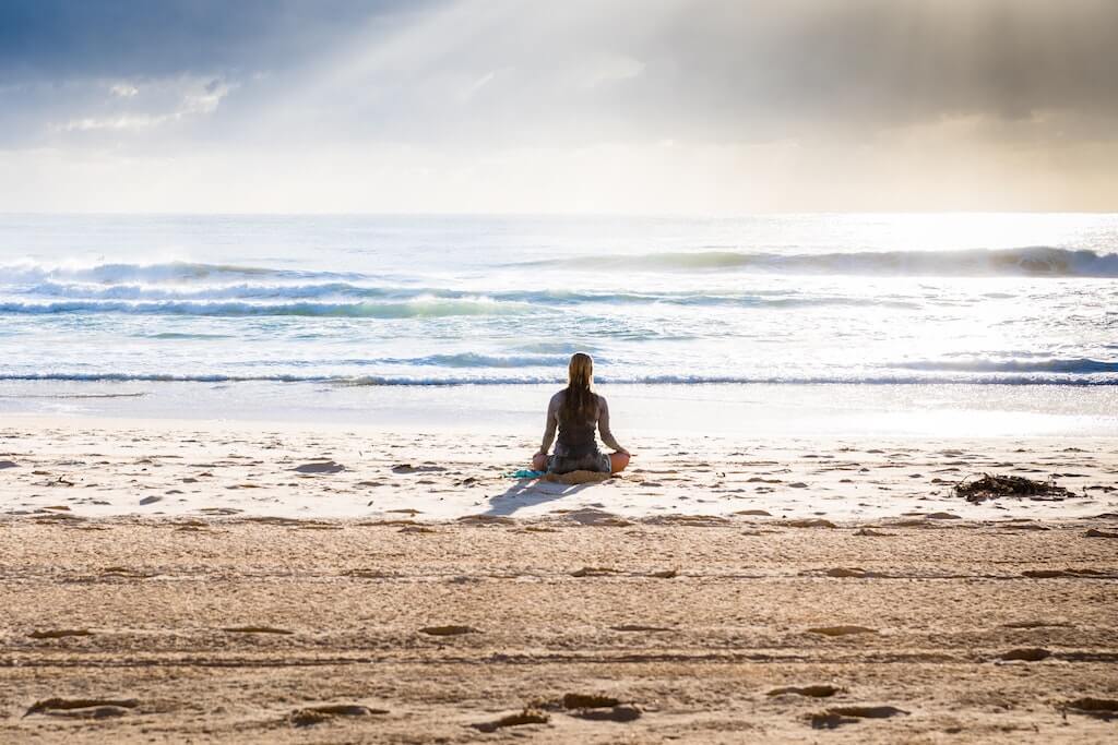travel and mental health woman on beach alone meditation island sun sand ocean sea