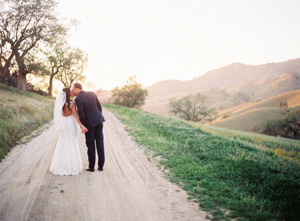 bride-in-keyhole-back-wedding-dress-kisses-groom-on-ranch