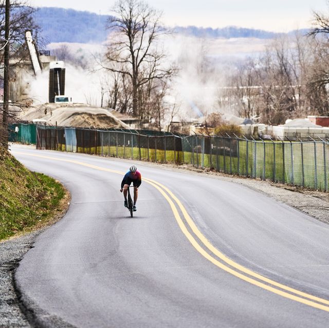 a person riding a bicycle on a road with a fence and trees