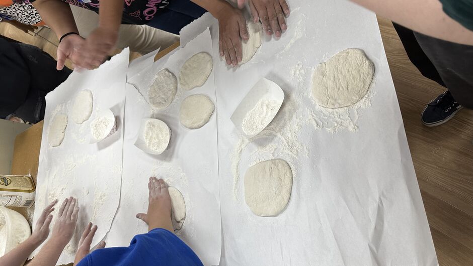 Many hands surround a table while molding and cooking bread