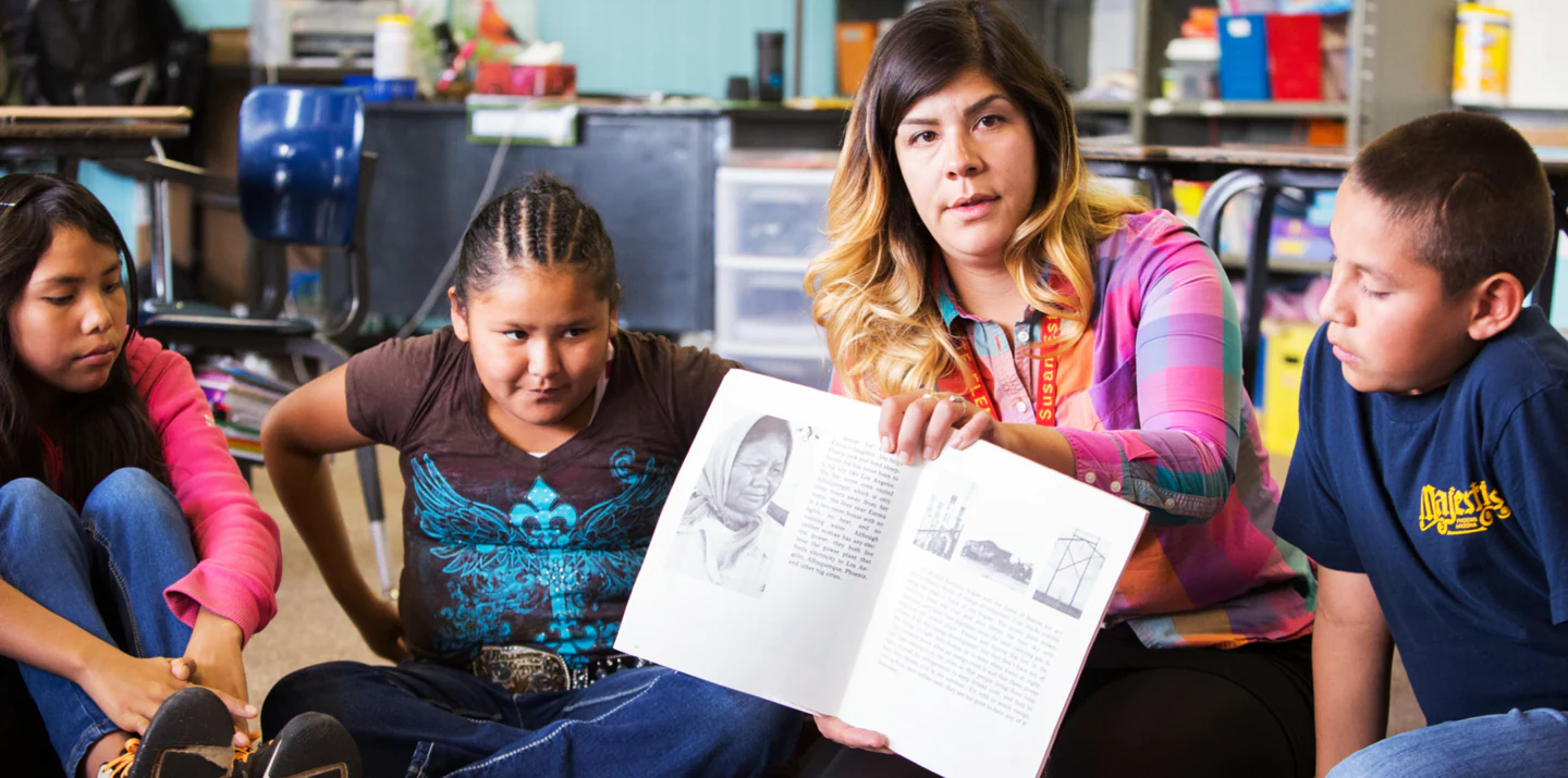 A teachers leads a reading assignment as students look on