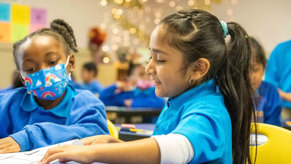 Two elementary girls share a notebook and read together in classroom